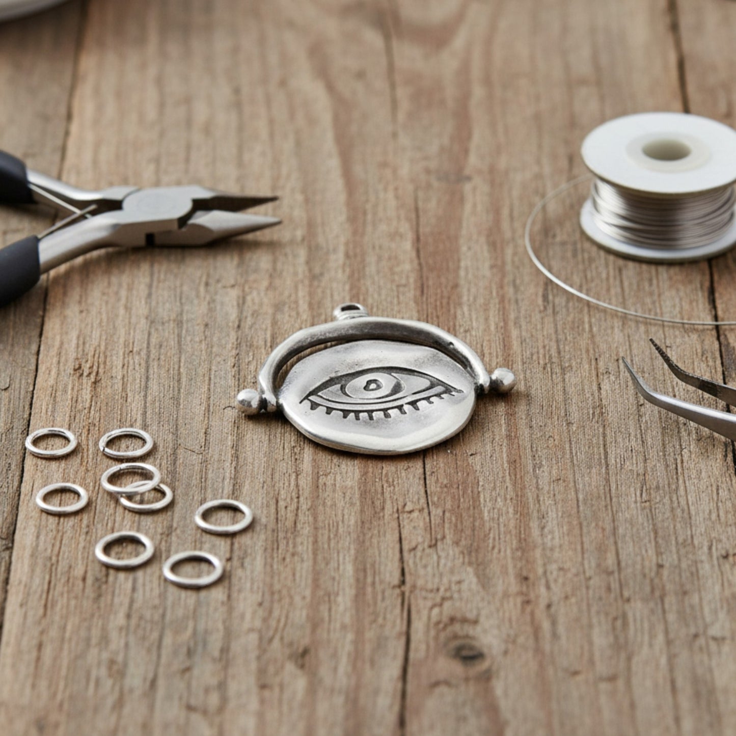 Hackberry Creek silver plated evil eye pendant with organic texture on a wooden workbench with jewelry making tools.