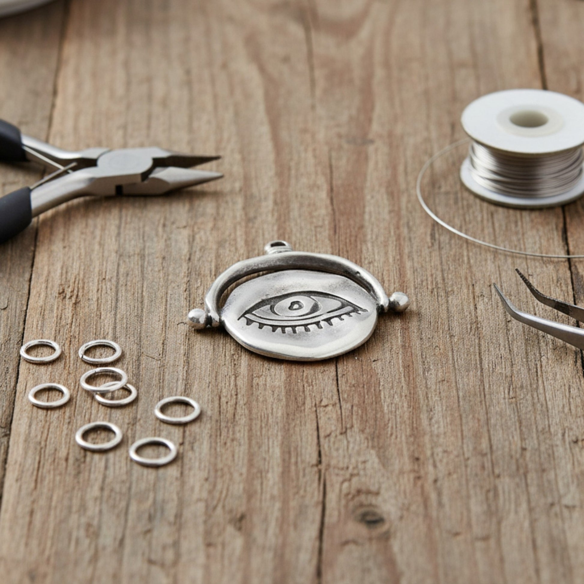 Hackberry Creek silver plated evil eye pendant with organic texture on a wooden workbench with jewelry making tools.