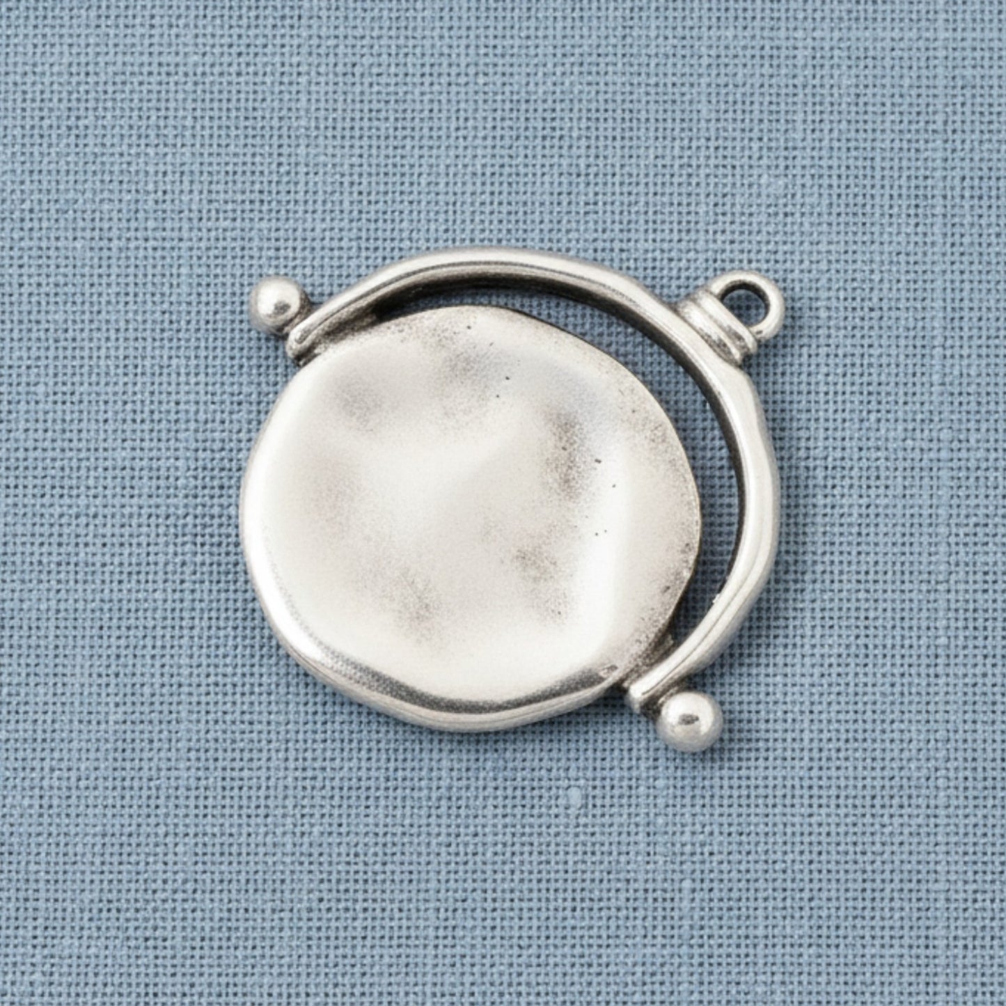 Hackberry Creek silver plated evil eye pendant with an organic hand-formed texture on a blue fabric background.