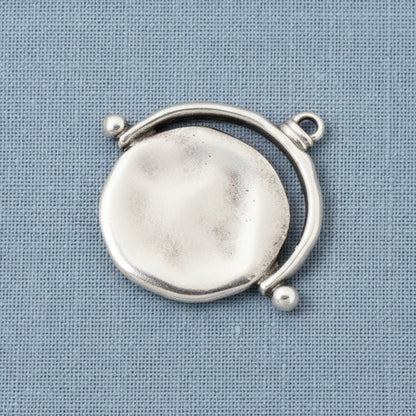 Hackberry Creek silver plated evil eye pendant with an organic hand-formed texture on a blue fabric background.