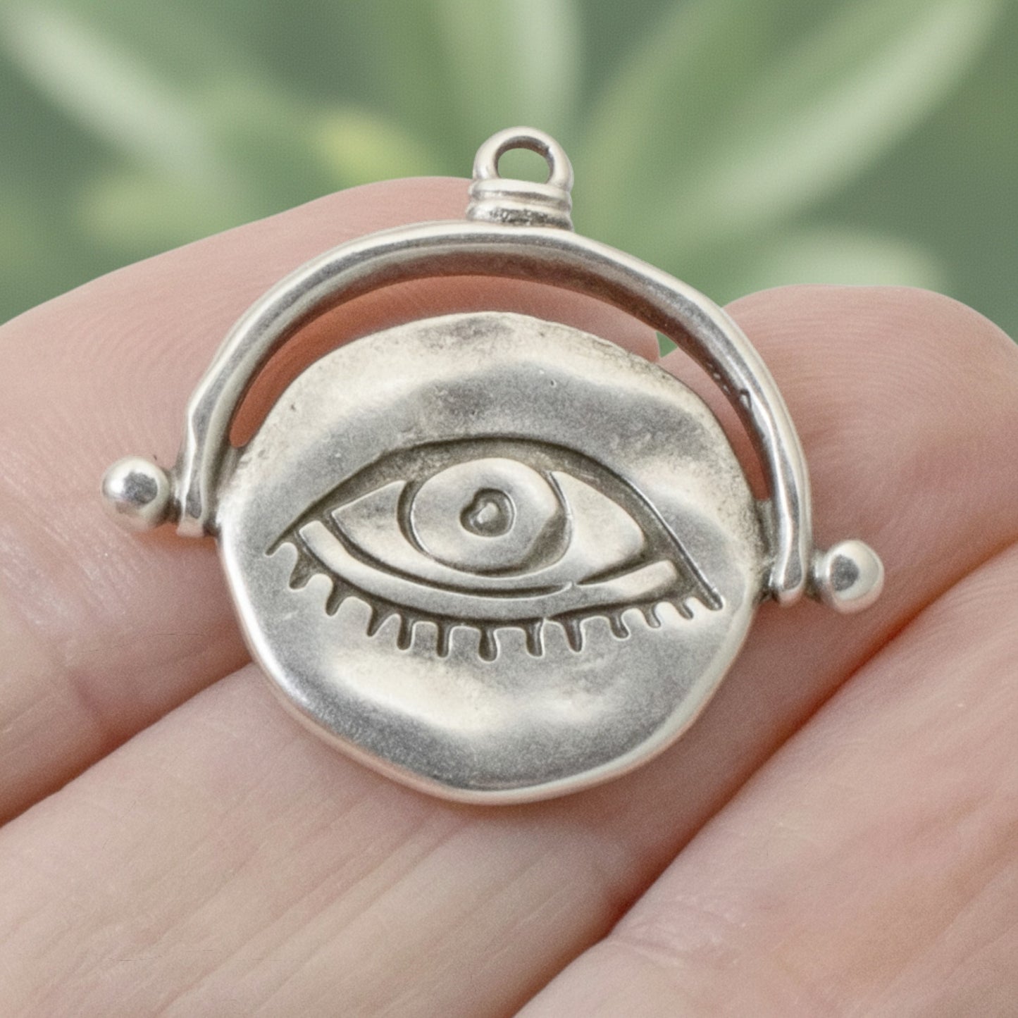 Hackberry Creek silver plated evil eye pendant with hand-formed texture held in a hand for scale.