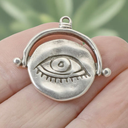 Hackberry Creek silver plated evil eye pendant with hand-formed texture held in a hand for scale.