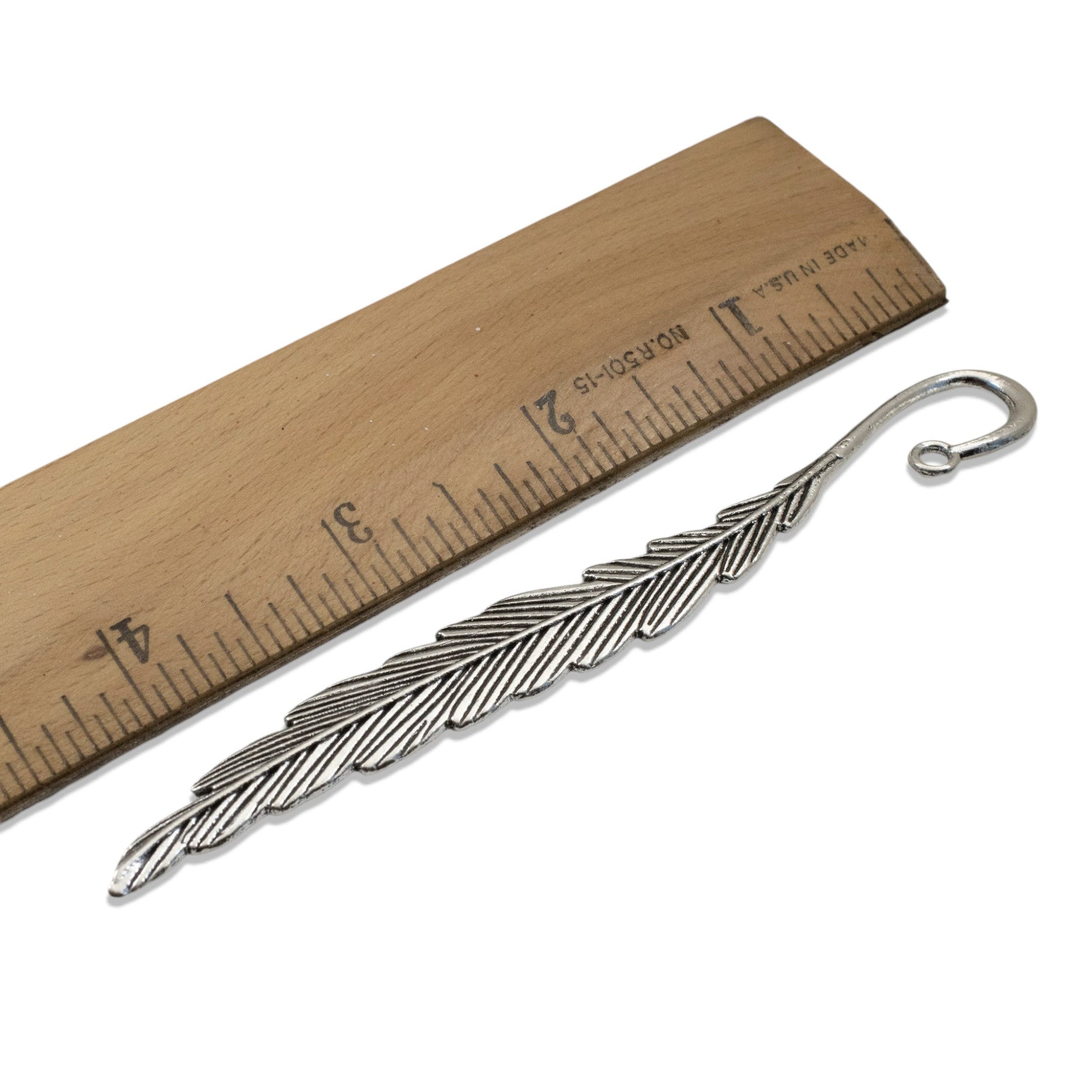 Hackberry Creek antique silver feather bookmark base with etched detail next to a wooden ruler for scale