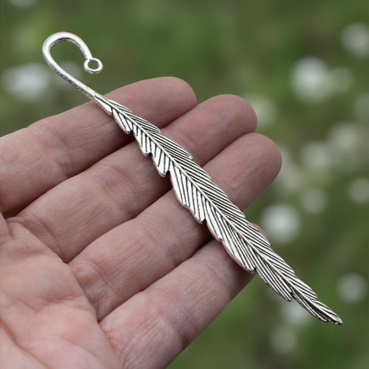 Hackberry Creek silver feather bookmark base with etched detail held in a hand for DIY charm projects.