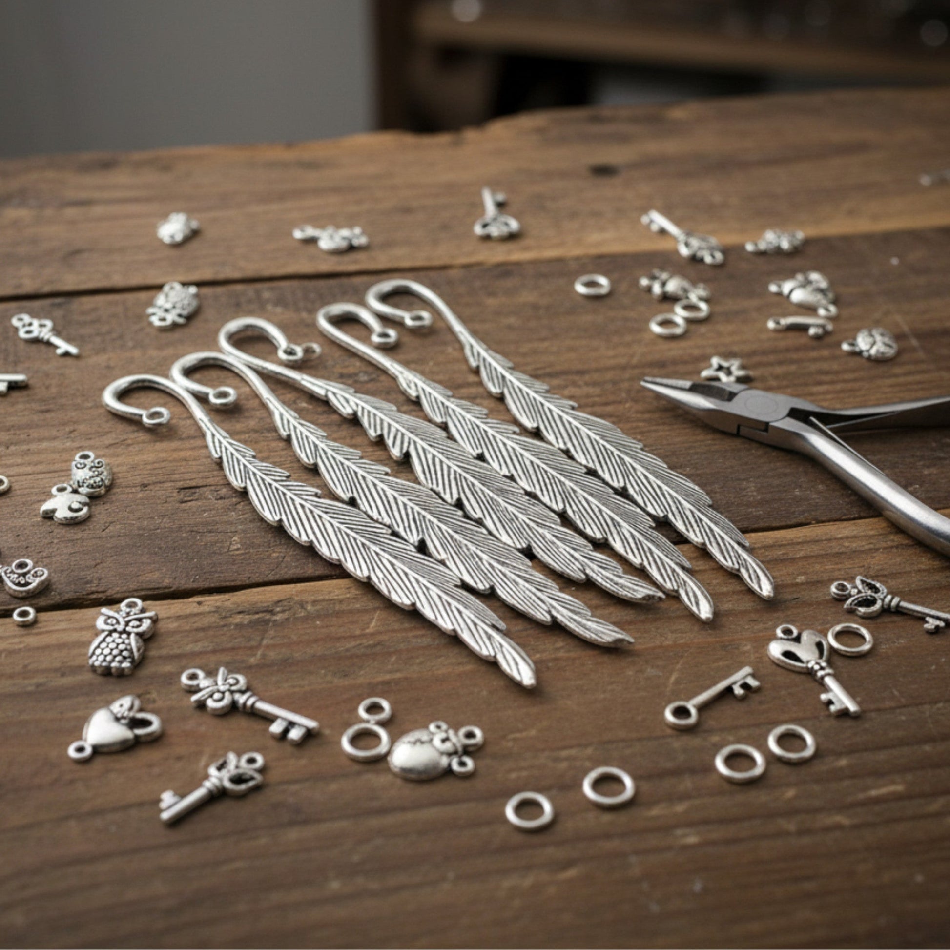 Hackberry Creek silver feather bookmark bases with assorted charms and pliers on a rustic wooden table