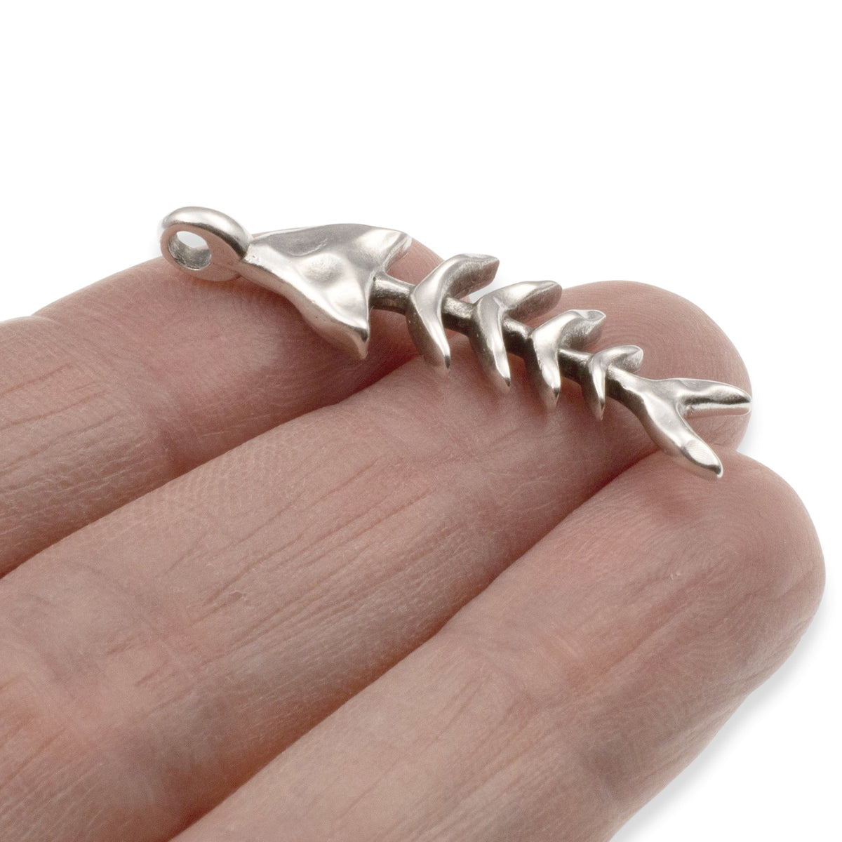 Hackberry Creek silver fishbone skeleton pendant held on a finger, featuring detailed antique finish coastal jewelry.