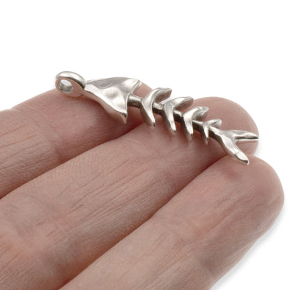 Hackberry Creek silver fishbone skeleton pendant held on a finger, featuring detailed antique finish coastal jewelry.