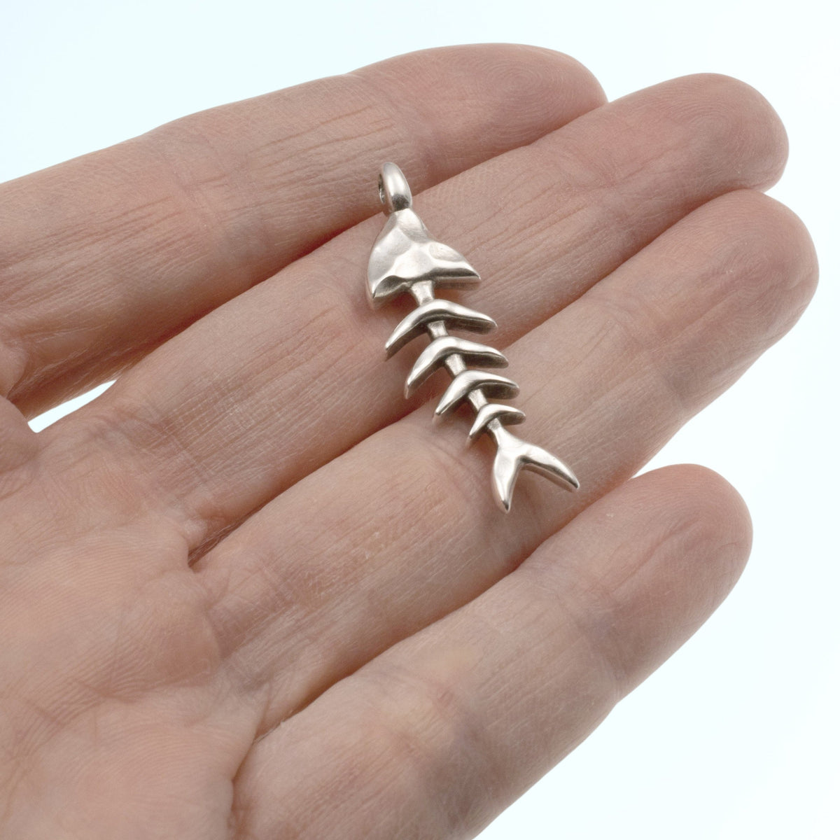 Hackberry Creek antique silver-plated fishbone skeleton pendant held in a hand for scale