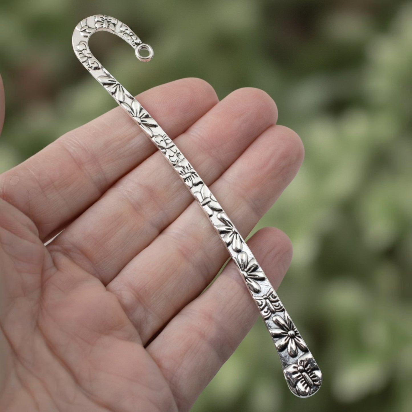 Hackberry Creek silver zinc alloy hook bookmark with raised floral and butterfly pattern held in a hand