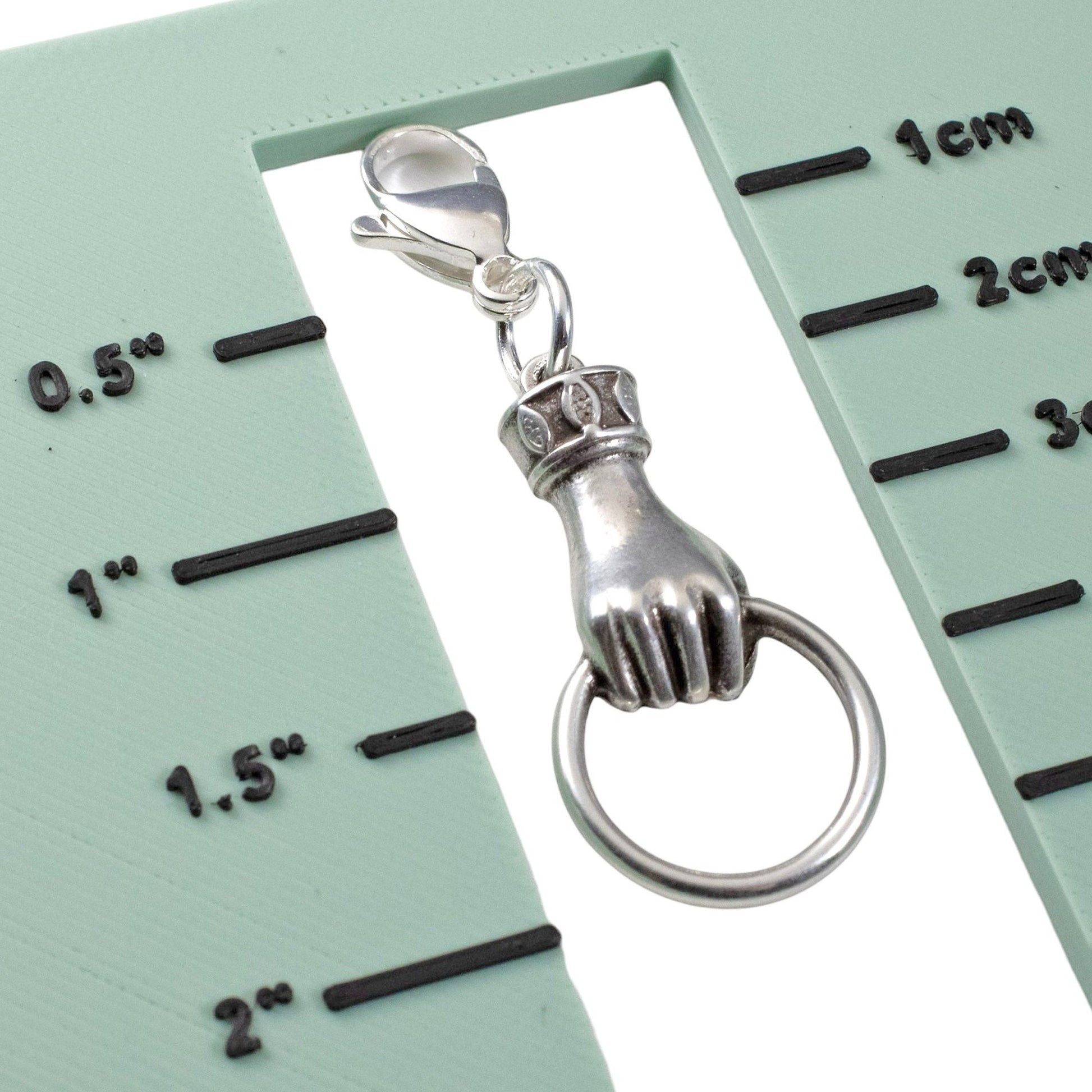 Hackberry Creek silver hand charm with ring holder and lobster clasp on a measurement scale for jewelry making