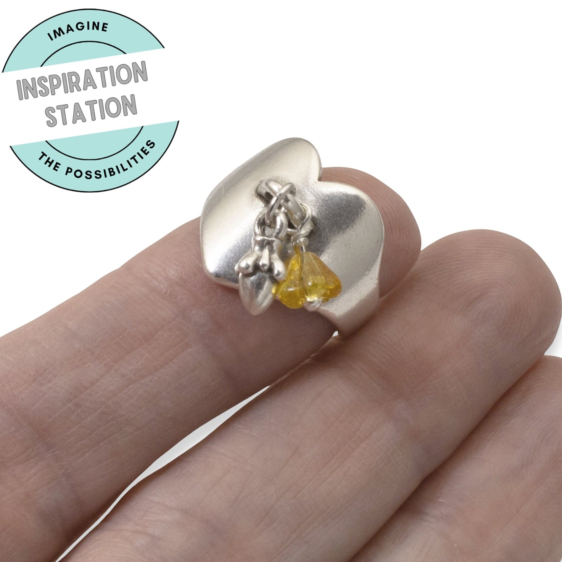 Hackberry Creek silver-plated heart ring base with a charm loop, worn on a finger with small yellow and silver charms.