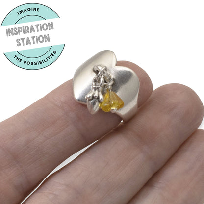 Hackberry Creek silver-plated heart ring base with a charm loop, worn on a finger with small yellow and silver charms.