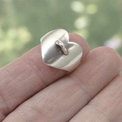 Hackberry Creek silver-plated heart-shaped adjustable ring base with a charm loop on a finger against a blurred background.