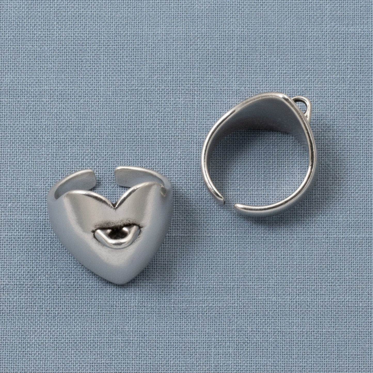 Hackberry Creek set of two silver-plated heart-shaped adjustable ring bases with charm loops on a blue fabric background.