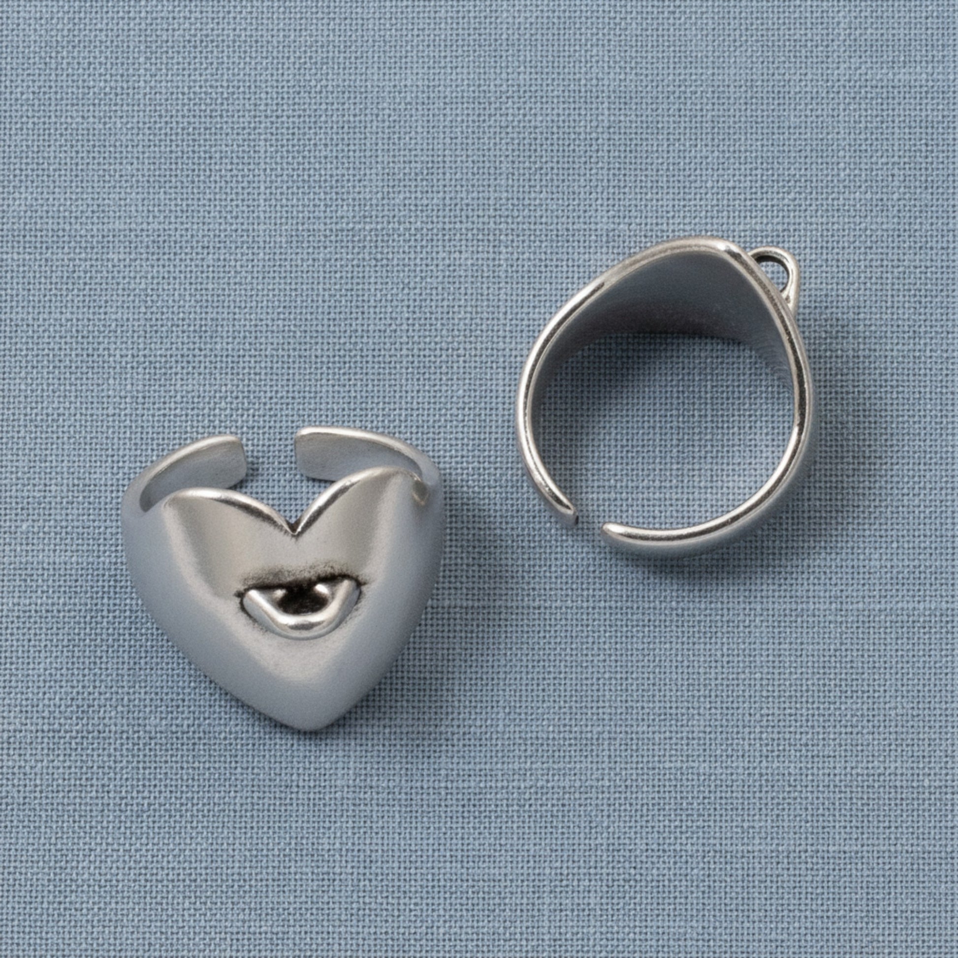 Hackberry Creek set of two silver-plated heart-shaped adjustable ring bases with charm loops on a blue fabric background.