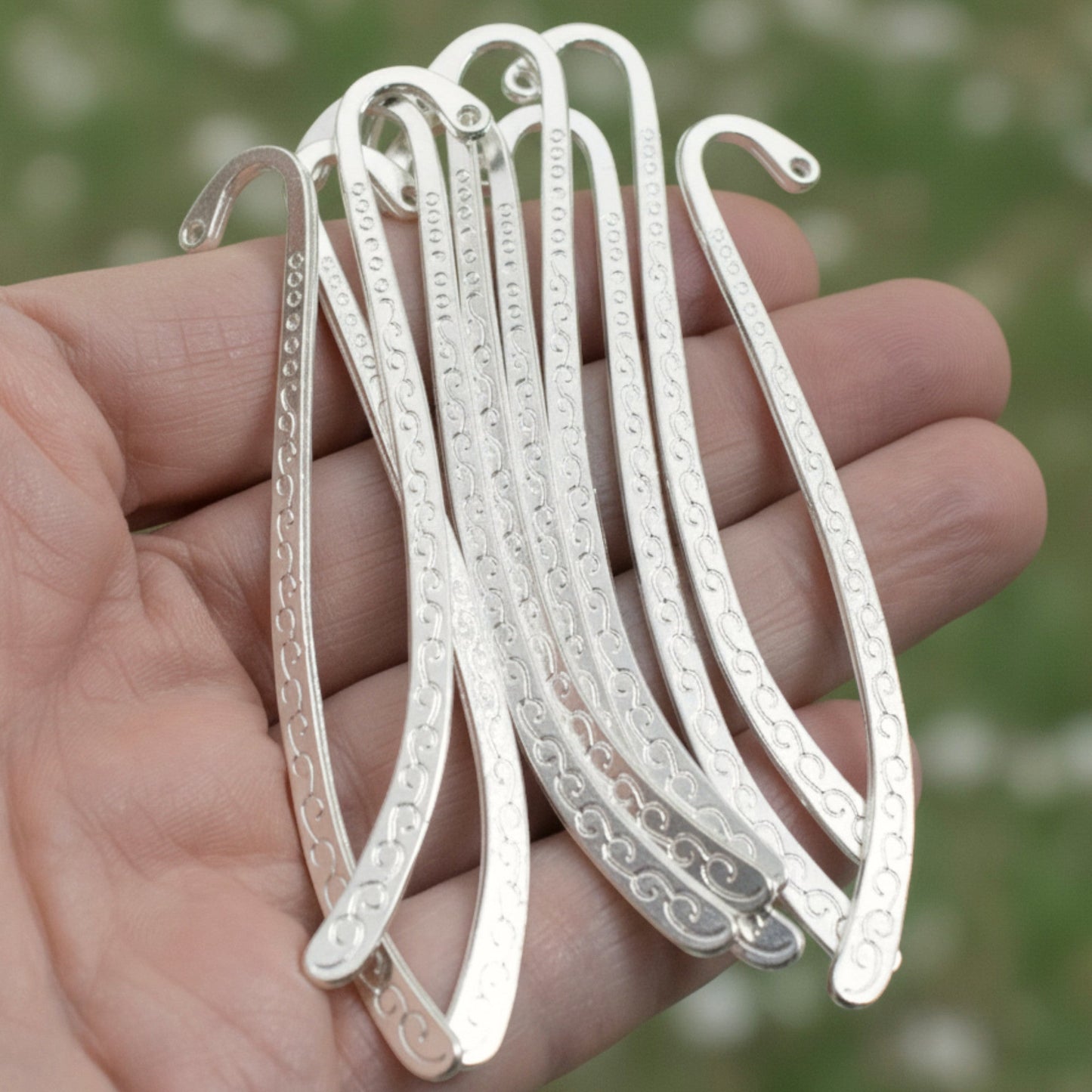 Hackberry Creek silver-tone metal hook bookmark blanks with Tibetan swirl detail held in a hand