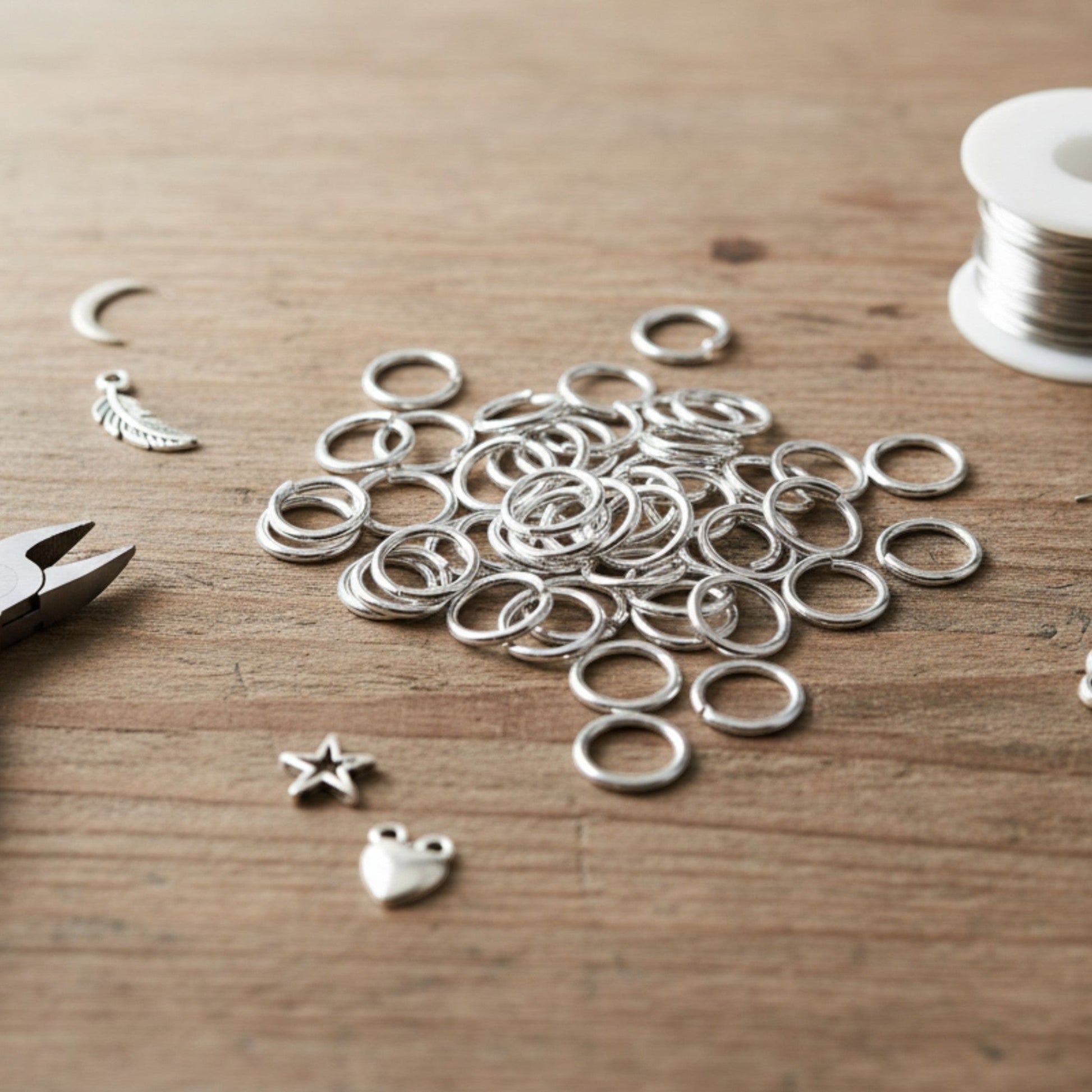 Hackberry Creek 8mm silver plated brass jump rings for jewelry making on a wooden table with charms and pliers