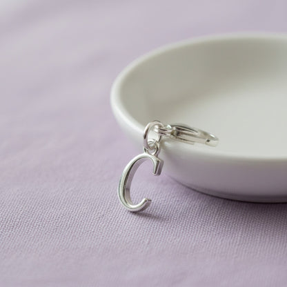 Hackberry Creek silver cursive letter C charm with a stainless steel lobster clasp on a white dish.