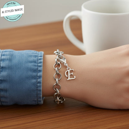 Hackberry Creek silver cursive letter E charm on a chain bracelet, worn on a wrist with a denim sleeve.