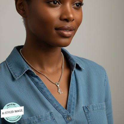 Hackberry Creek silver cursive letter E charm on a ball chain necklace worn by a woman in a blue denim shirt.