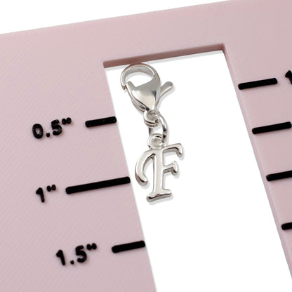 Hackberry Creek silver cursive letter F charm with lobster clasp shown against a scale for size reference.
