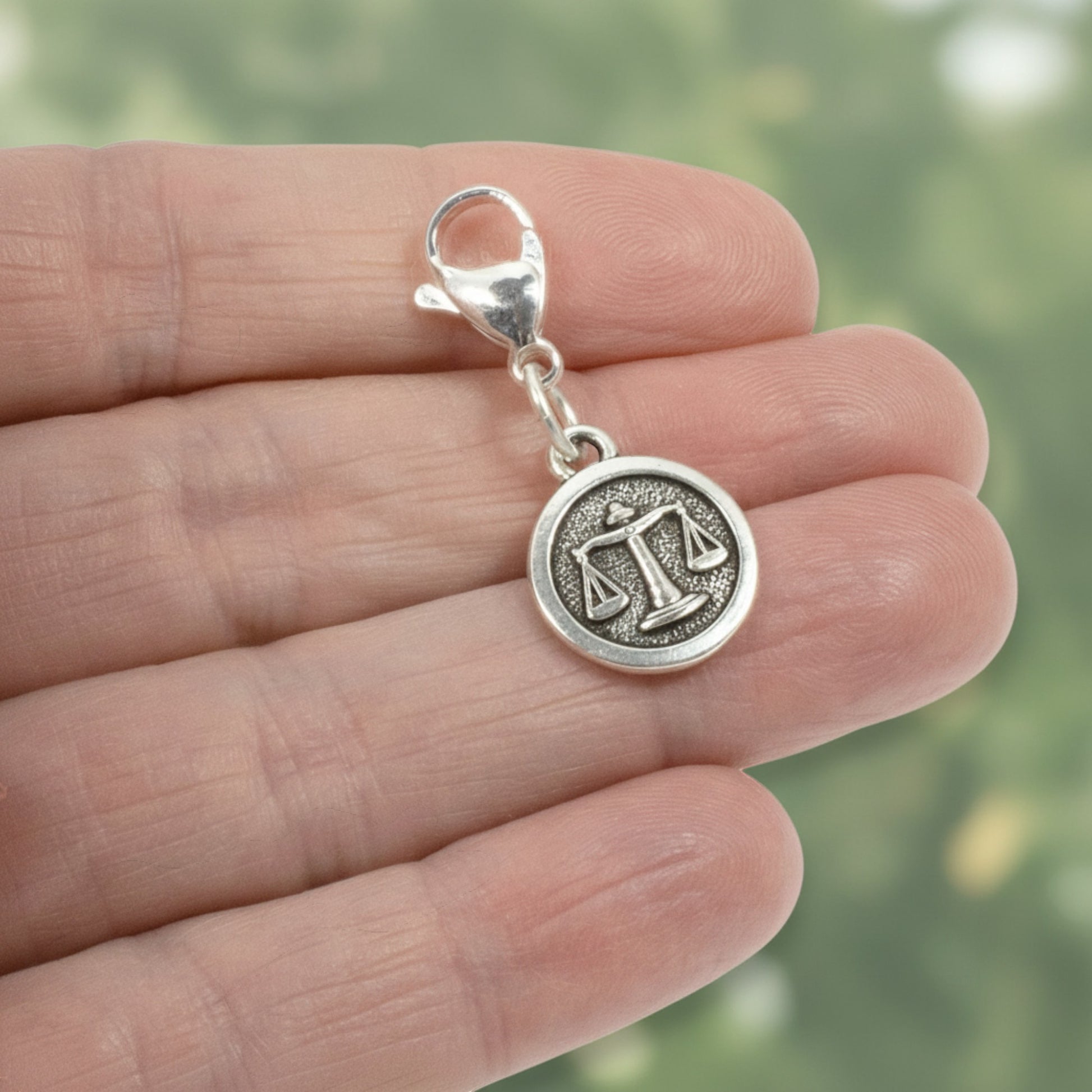 Hackberry Creek silver Libra zodiac charm with scales design and lobster clasp held in a hand.