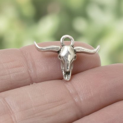 Hackberry Creek silver longhorn steer skull charm held on a finger, featuring antique oxidized finish for boho jewelry