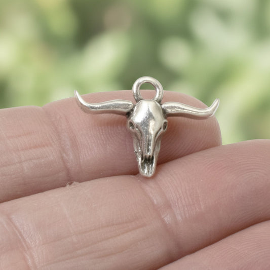 Hackberry Creek silver longhorn steer skull charm held on a finger, featuring antique oxidized finish for boho jewelry