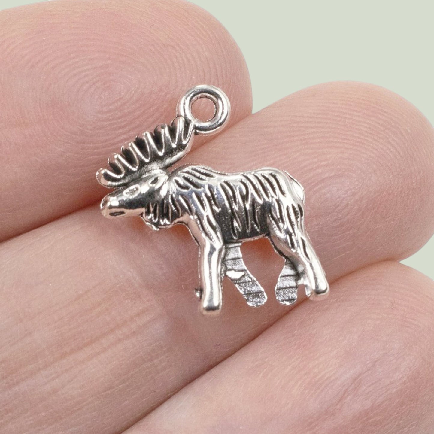 Hackberry Creek silver moose charm pendant with detailed walking posture held between fingers for scale