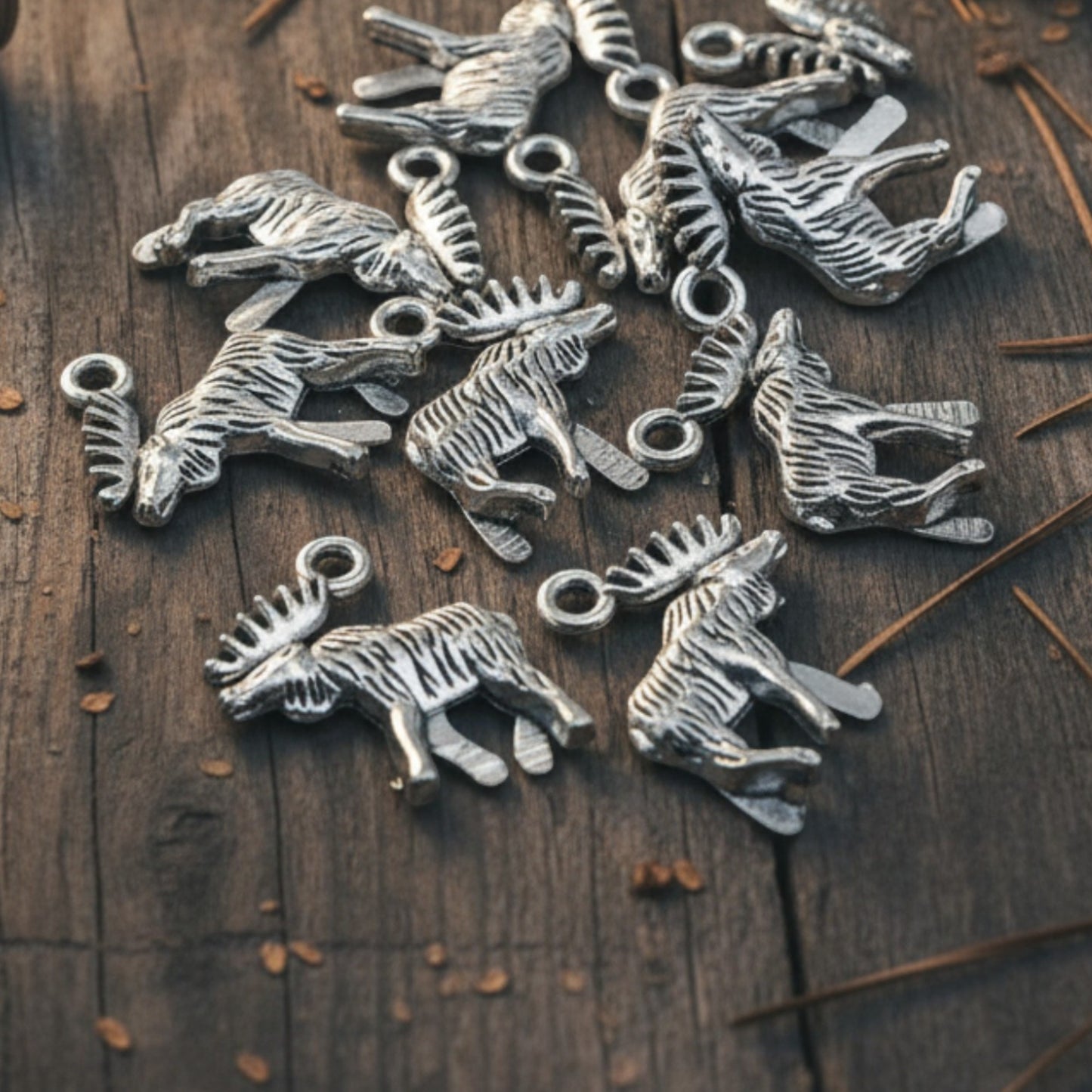 Hackberry Creek silver moose and elk metal charms for jewelry making, displayed on a rustic wooden table with tools.
