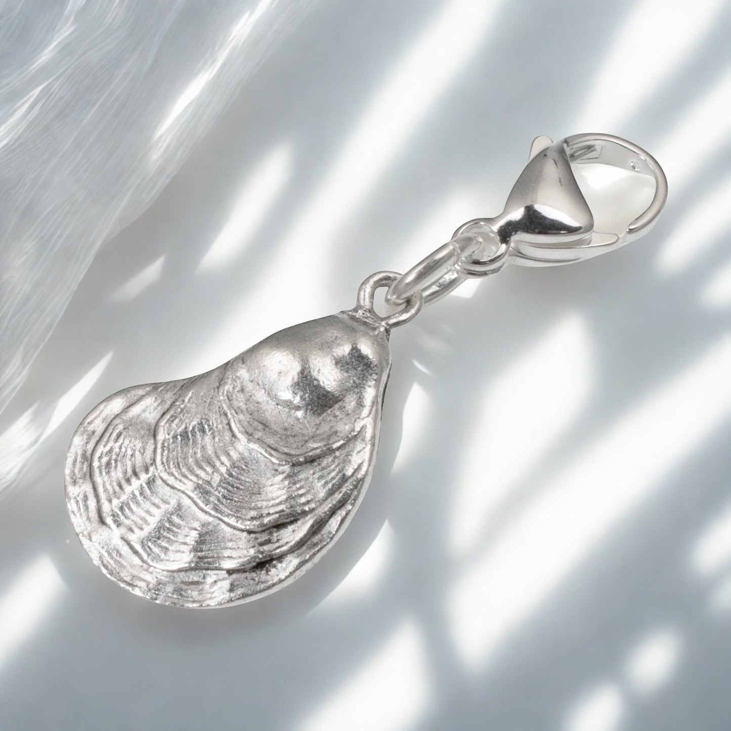 Hackberry Creek silver oyster shell charm with a lobster clasp, featuring detailed 3D texture for coastal jewelry.