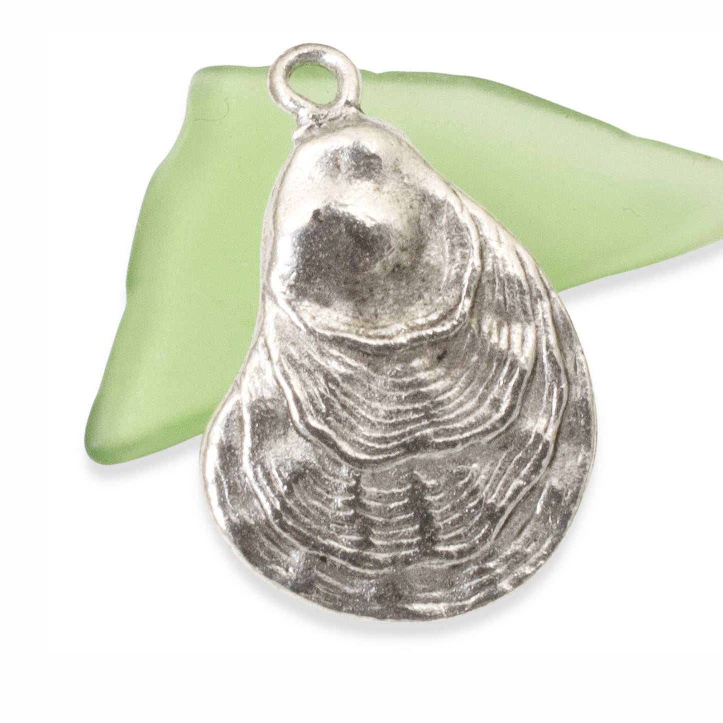 Hackberry Creek antique silver oyster shell charm pendant with detailed texture resting on a piece of sea glass