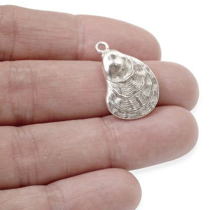 Hackberry Creek silver oyster shell charm held in a hand, featuring detailed antique finish and coastal design.