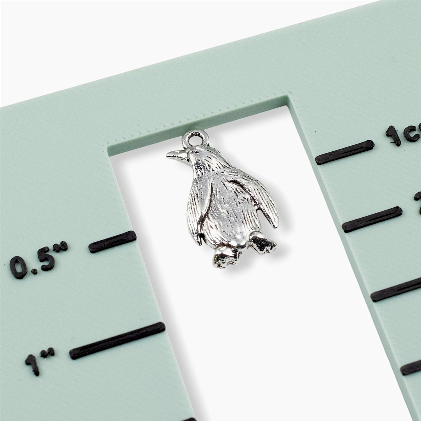 Hackberry Creek silver metal penguin charm with detailed feather texture shown against a green measurement guide.