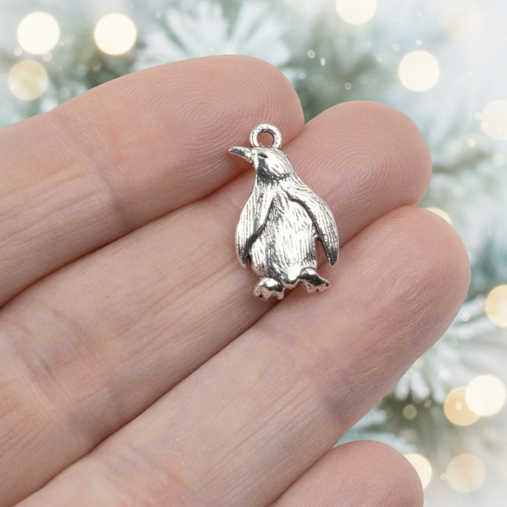 Hackberry Creek silver metal penguin charm with detailed feather texture held between fingers for scale