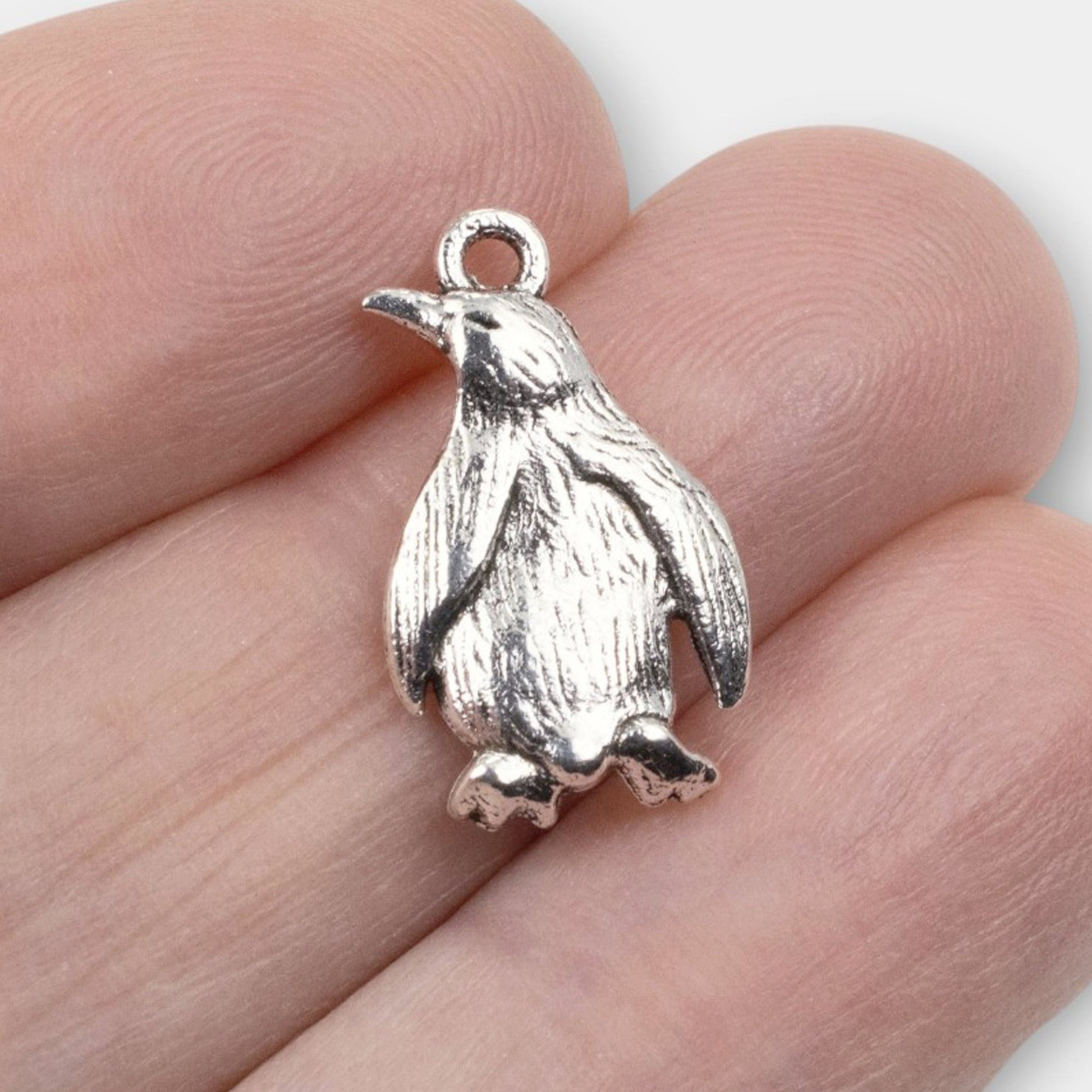Hackberry Creek silver metal penguin charm with detailed feather texture held between fingers for scale