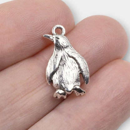 Hackberry Creek silver metal penguin charm with detailed feather texture held between fingers for scale