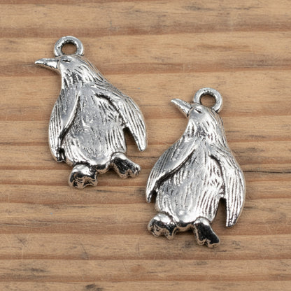 Hackberry Creek silver metal penguin charms with detailed feather texture for jewelry making on a wooden surface
