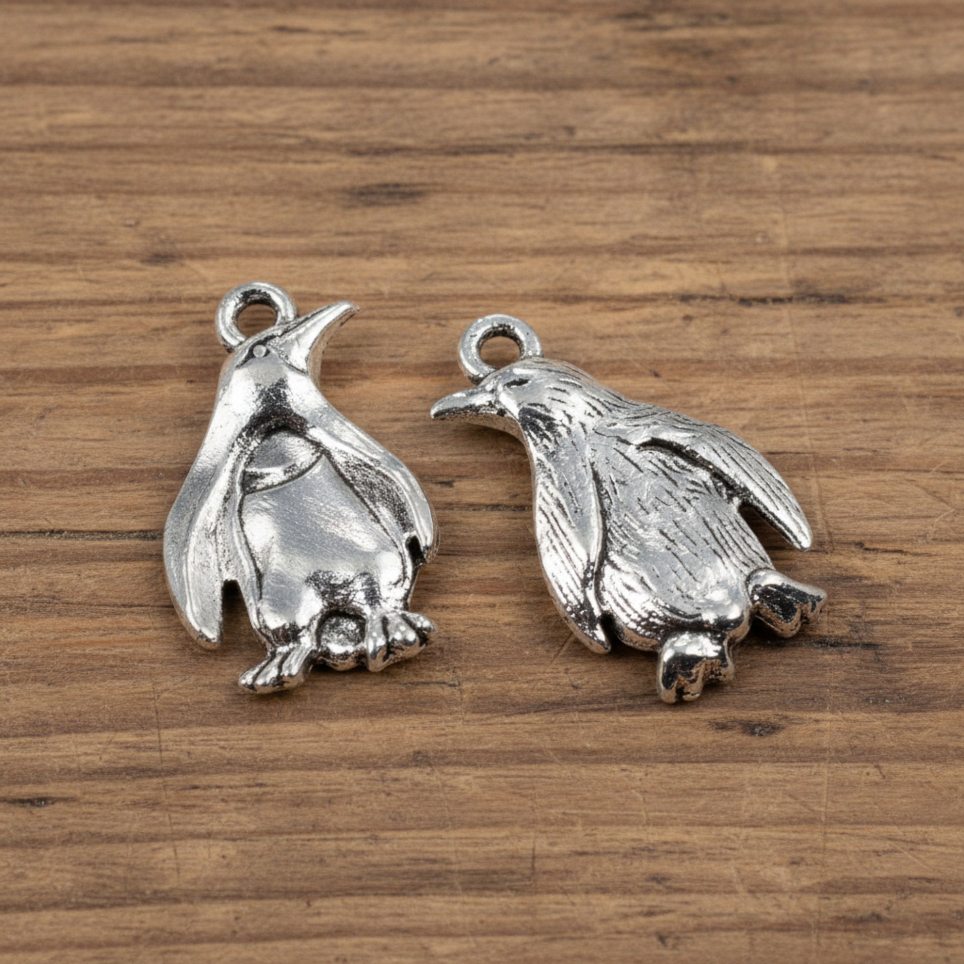 Hackberry Creek silver penguin charms with detailed feather texture on a rustic wooden background