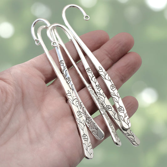 Hackberry Creek antique silver rose and vine metal bookmark bases held in a hand for DIY craft projects.