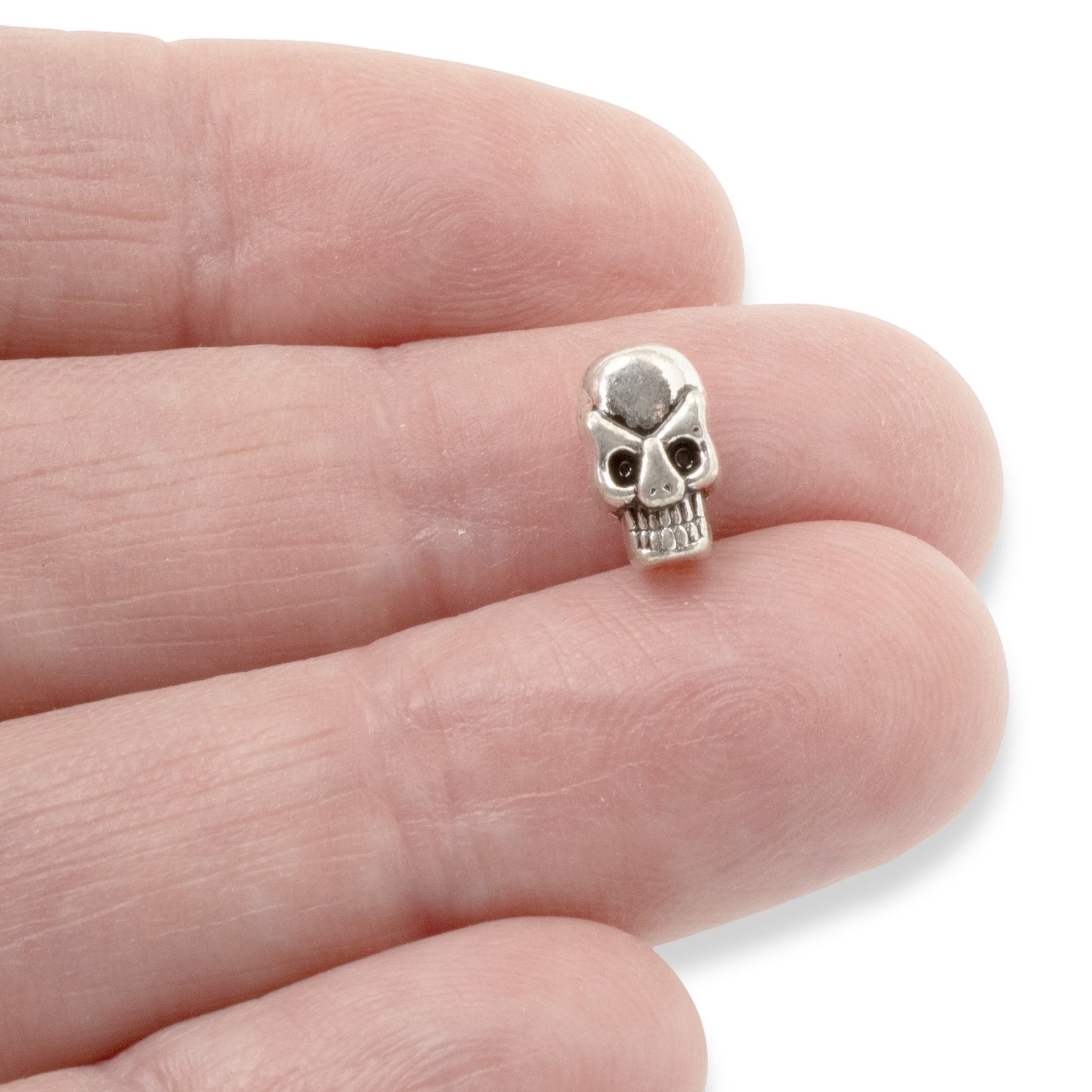 Hackberry Creek antique silver 3D skull alloy bead held between fingers for scale in jewelry making