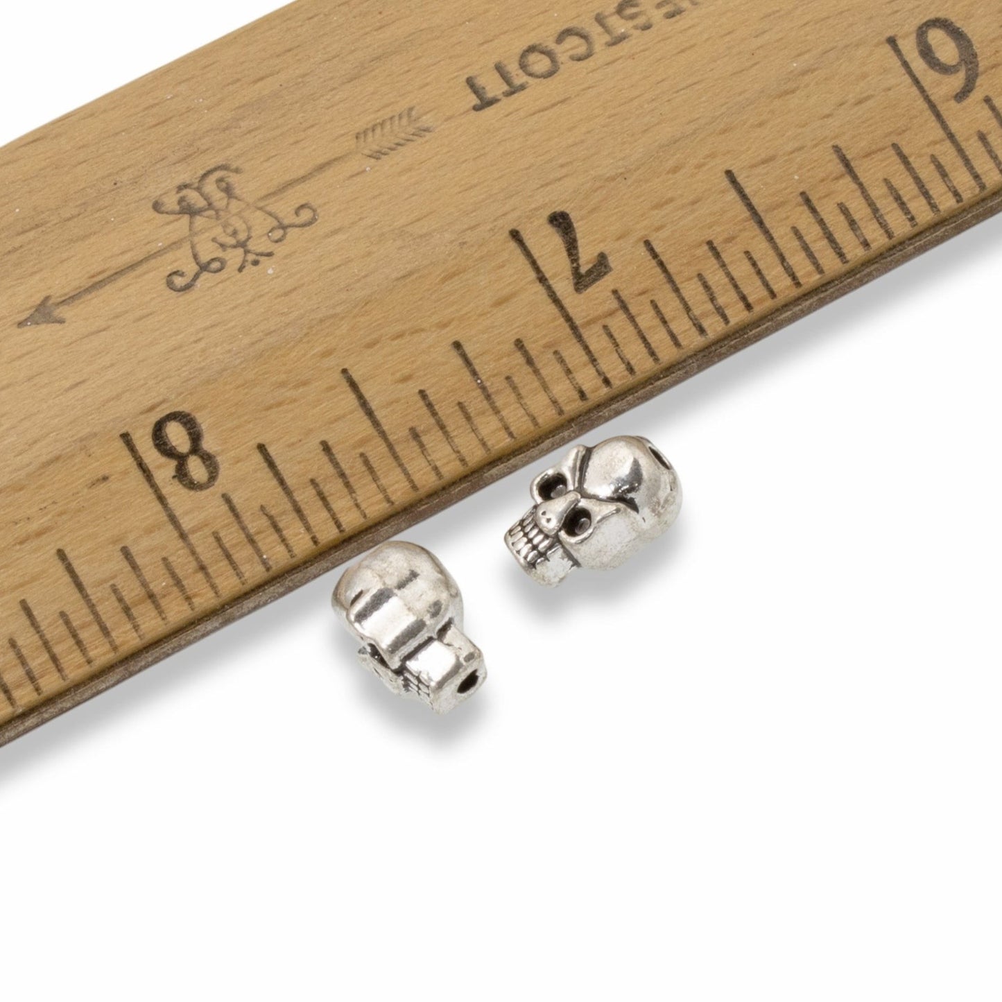 Hackberry Creek antique silver 3D skull beads for jewelry making shown next to a wooden ruler for scale