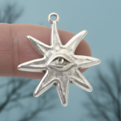 Hackberry Creek silver star eye pendant held on a finger against a blurred outdoor background