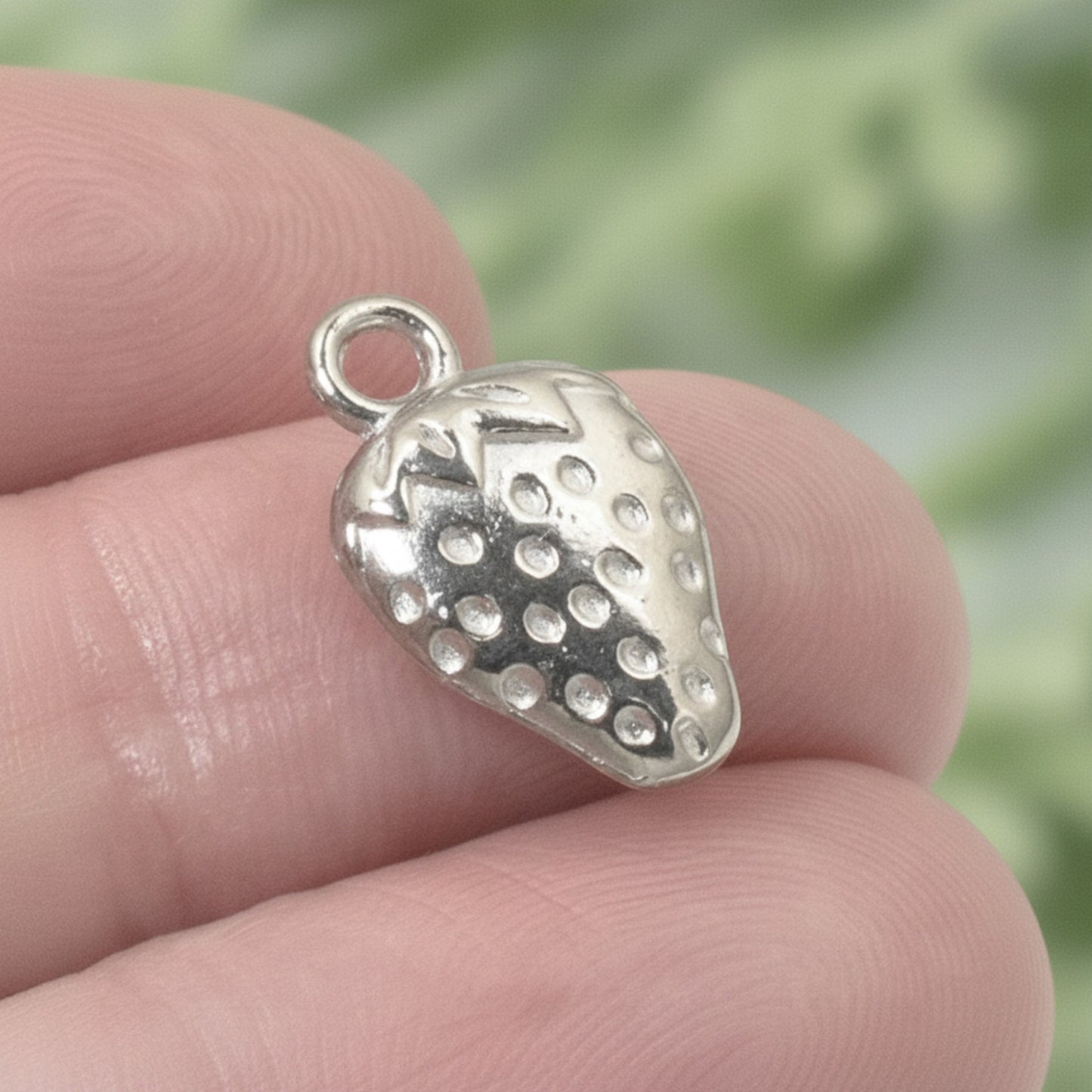 Silver strawberry charm with textured surface and a hanging loop. Ideal for jewelry making and gifts.