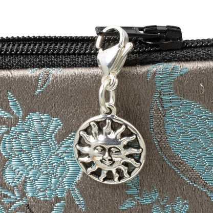 Hackberry Creek silver sun charm with a lobster clasp attached to a patterned zipper pull on a bag