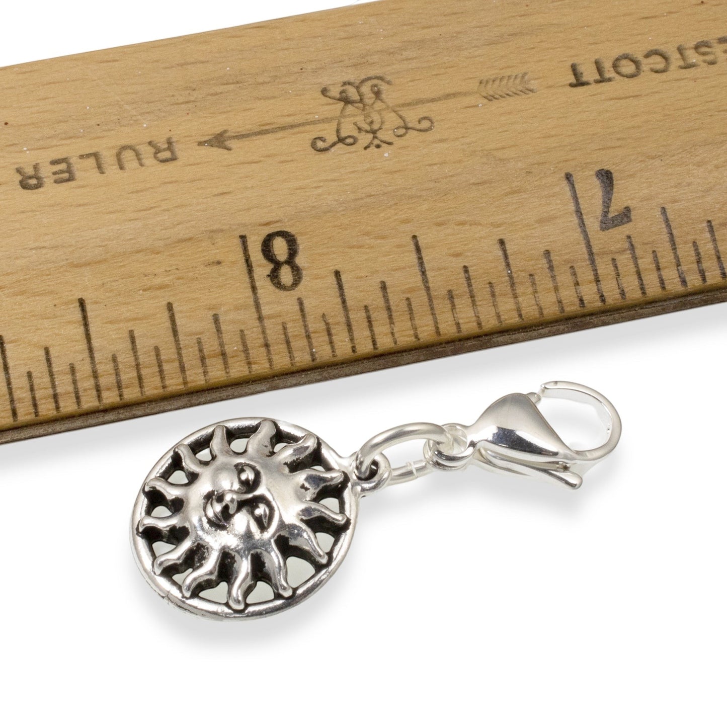 Hackberry Creek silver sun charm with lobster clasp next to a wooden ruler for scale