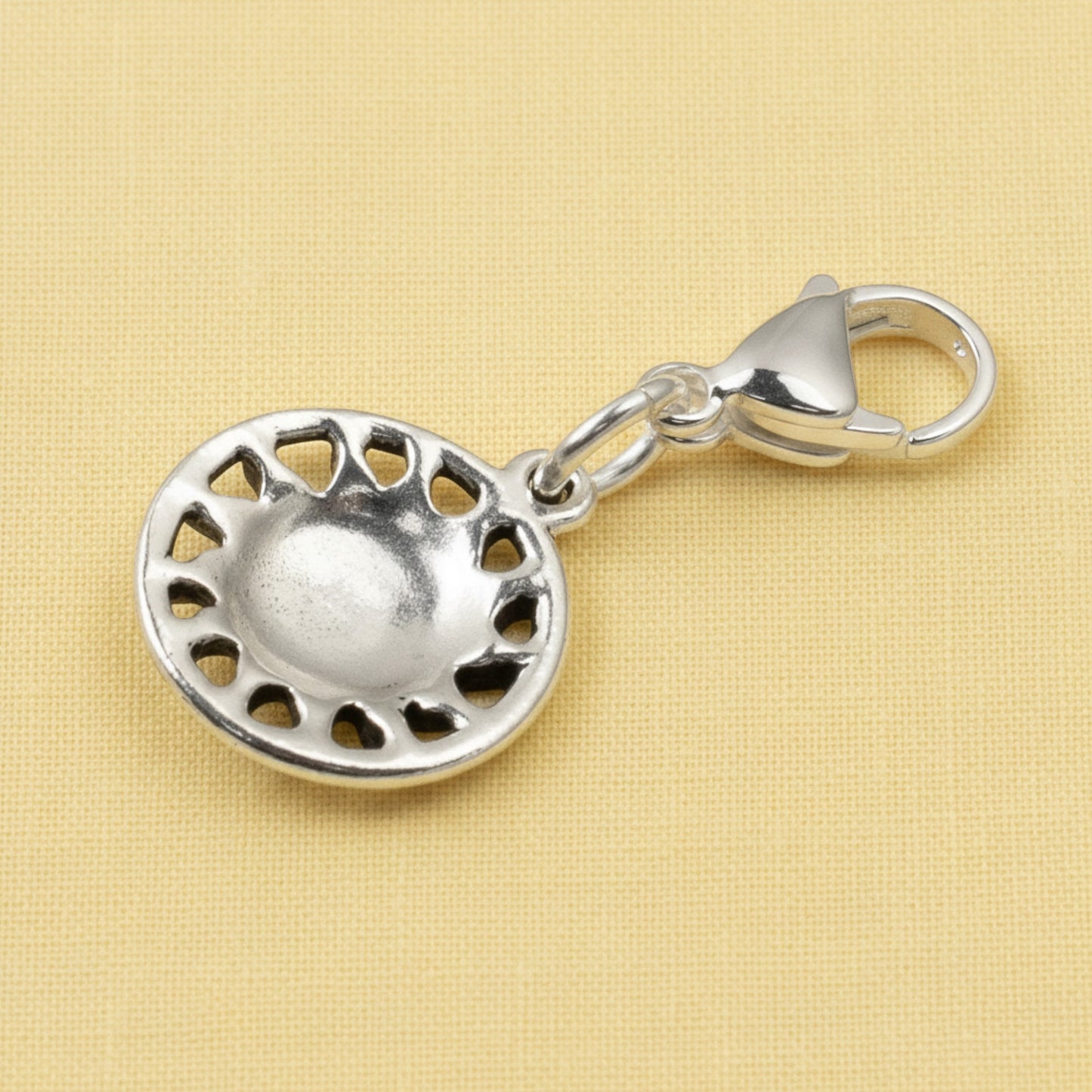 Hackberry Creek silver sun charm with lobster clasp for bags and keychains on a textured yellow background