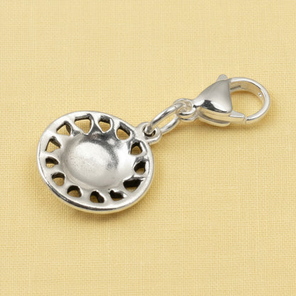 Hackberry Creek silver sun charm with lobster clasp for bags and keychains on a textured yellow background