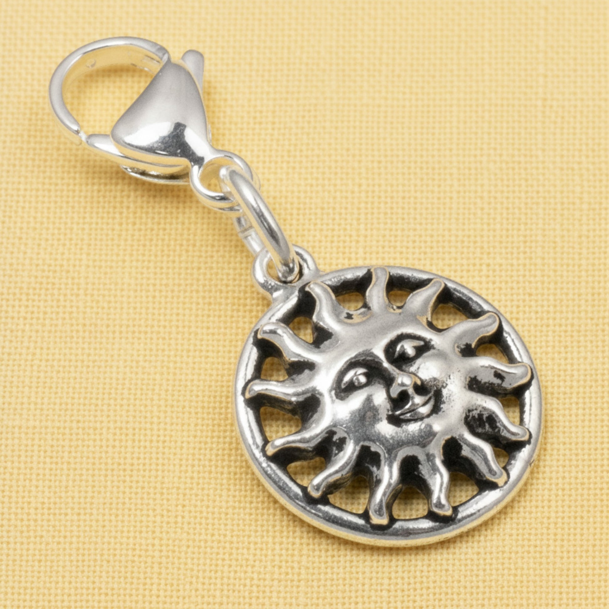 Hackberry Creek silver sun charm with a detailed face and stainless steel lobster clasp on a yellow background.