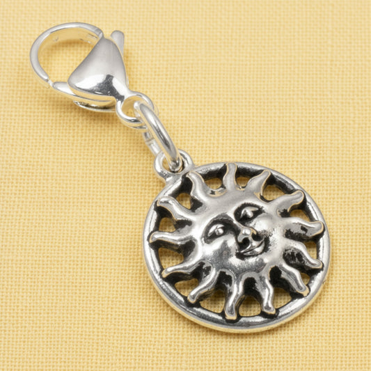 Hackberry Creek silver sun charm with a detailed face and stainless steel lobster clasp on a yellow background.